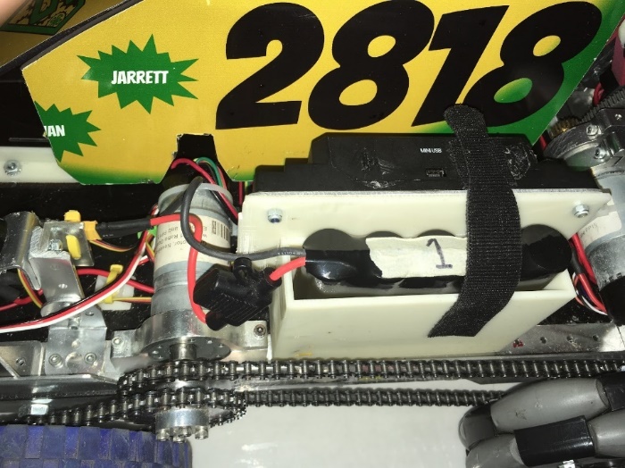 A battery secured in a white 3D-printed enclosure, with the yellow XT30 power connector zip-tied in place.