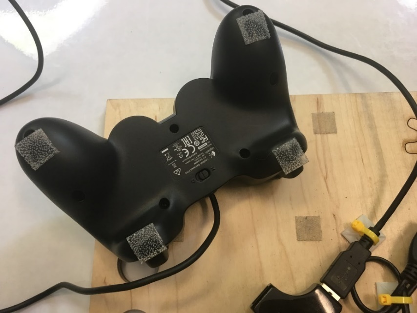 The back of two game controllers attached to a plywood board using hook-and-loop fasteners.