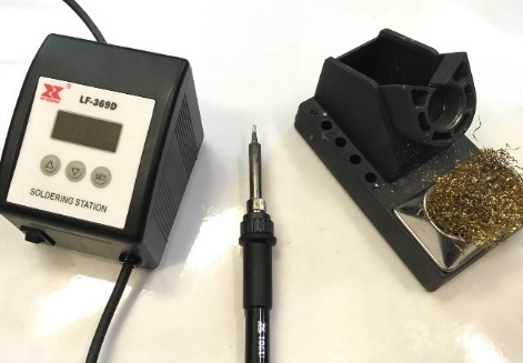 A temperature-controlled soldering station with an iron and stand next to a coil of solder.