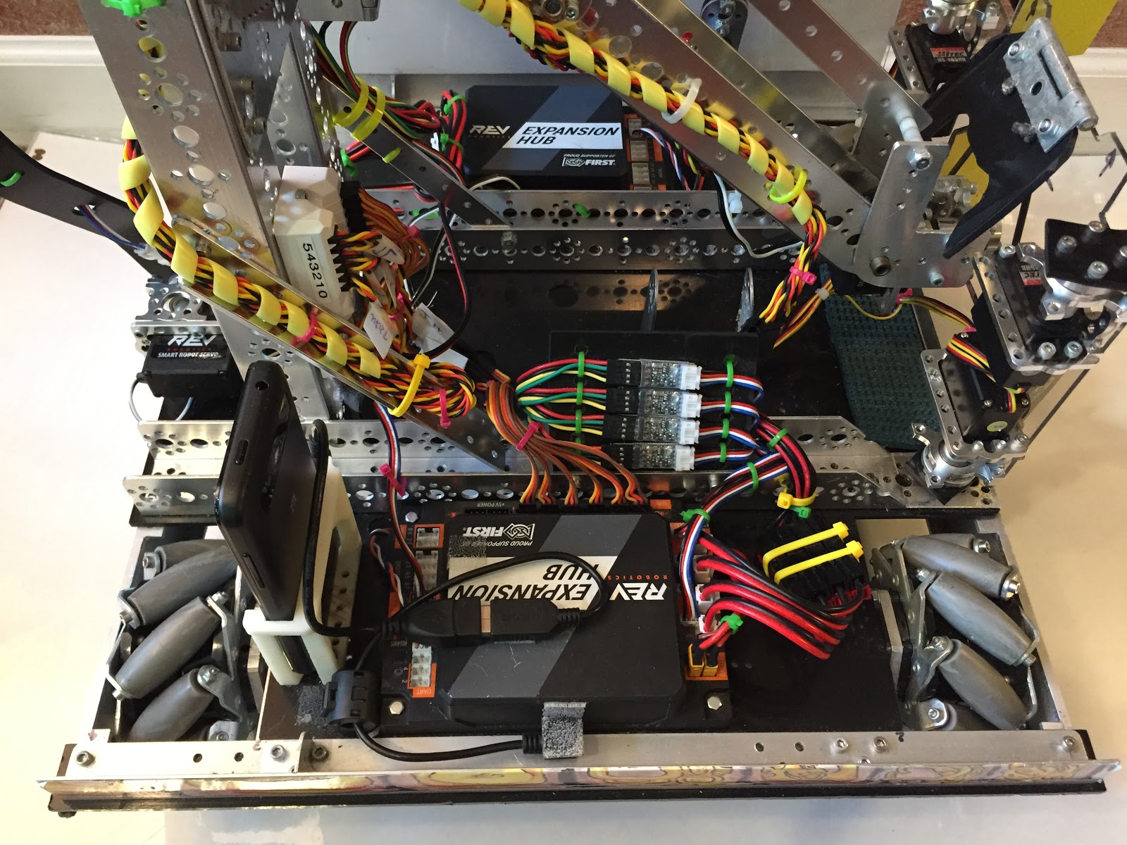 The underside of a robot showing many bundled and labeled wires, including yellow spiral-wrapped servo wiring, an Expansion Hub, and encoder level converter modules.